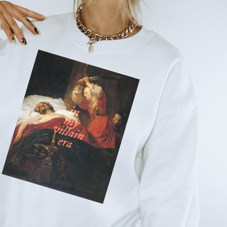 A white book lover sweatshirt featuring a painting of a woman and a sword with the text 'in my villain era'. The perfect bookish gift.