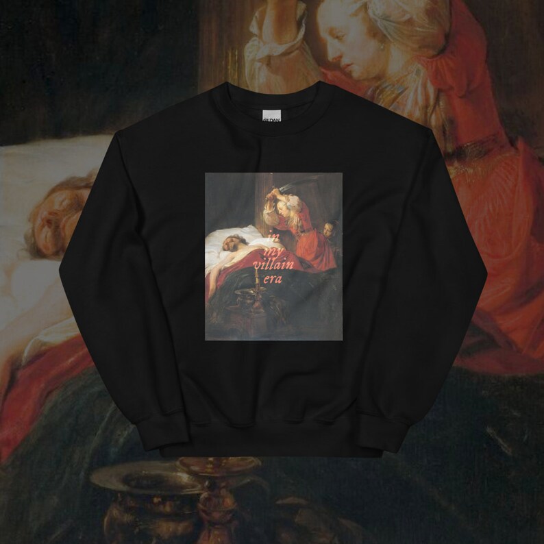 May include: Black sweatshirt with a painting of a woman holding a knife over a man in bed. The text "in my villain era" is printed in pink on the sweatshirt.