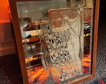 May include: A vintage wooden framed mirror with a decorative etched design of a woman standing next to a peacock. The mirror is on a rug with red, blue, and orange colors.