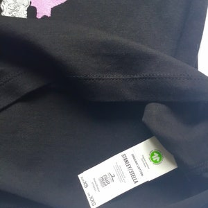 May include: Black t-shirt with a pink graphic print. The tag reads "Stanley/Stella" and "Organic Cotton" with a Global Organic Textile Standard (GOTS) certification logo. The size tag reads "EUR XS, US XXS".