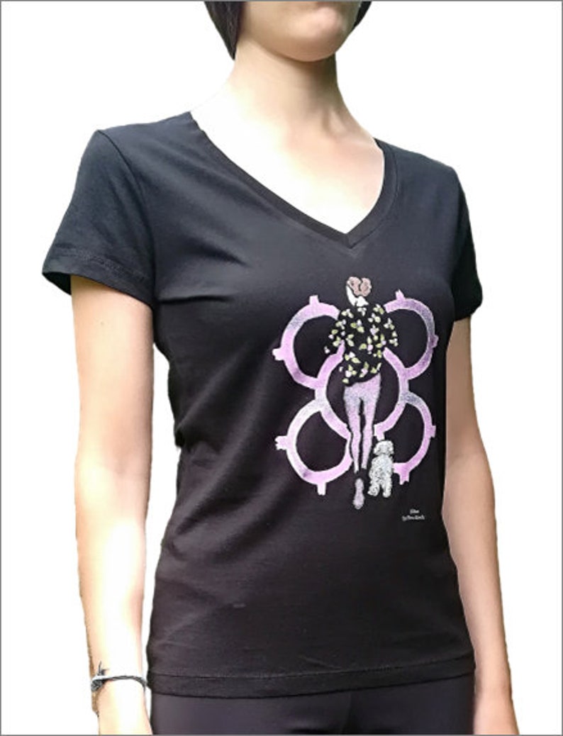 May include: Black v-neck t-shirt with a pink and green graphic print of a woman walking a small white dog. The graphic features a stylized design of interlocking circles.