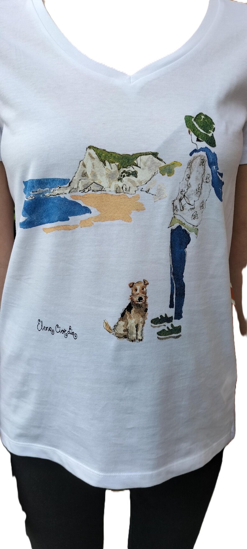May include: White t-shirt with a watercolor illustration of a person walking a dog on a beach. The illustration includes a cliff, ocean, and the text "Elena Ciortan".