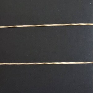 May include: Two gold chains on a black background. The chains are thin and delicate, with a simple design.
