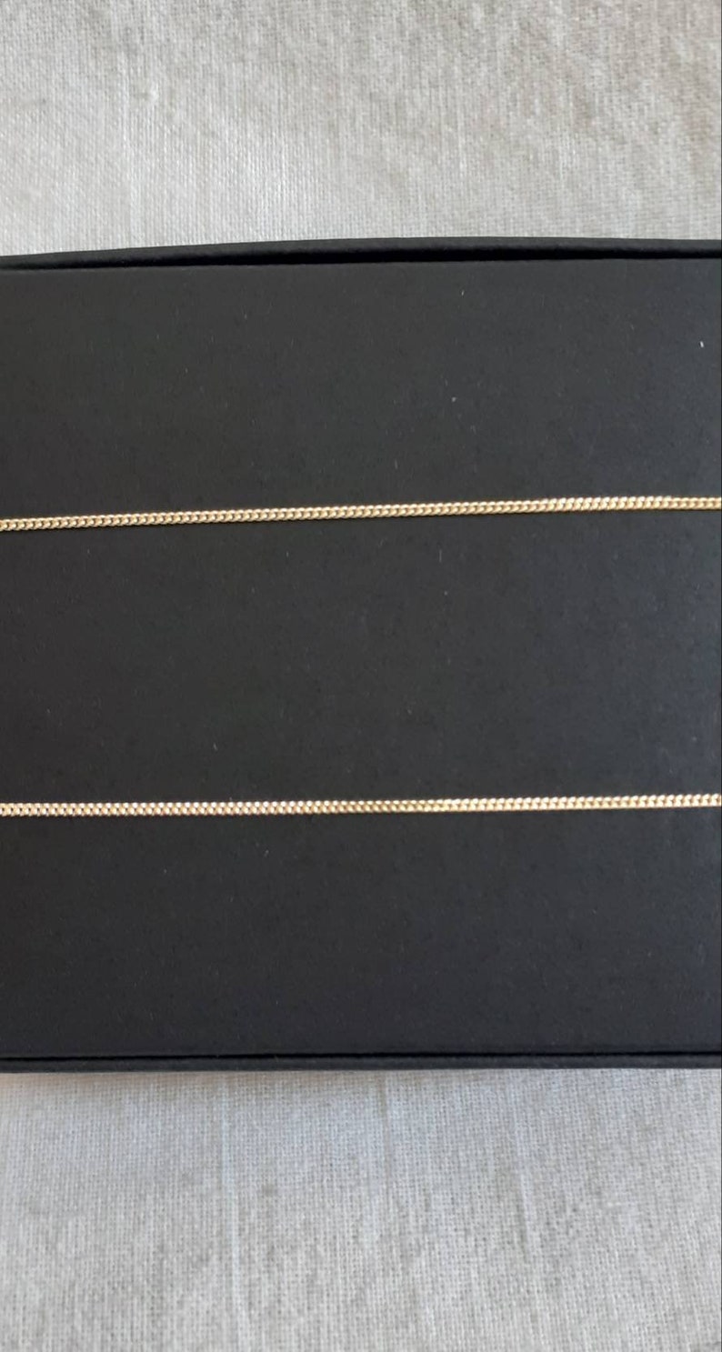 May include: Two gold chains on a black background. The chains are thin and delicate, with a simple design.