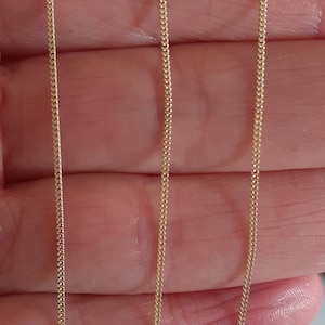 May include: Two gold chains, one on each side of the image, are shown against a light pink background. The chains are both the same length and have a delicate, fine link design.