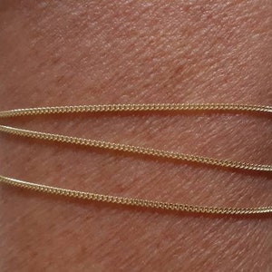 May include: A gold chain bracelet with a delicate, thin design. The bracelet is layered three times on a person's wrist.