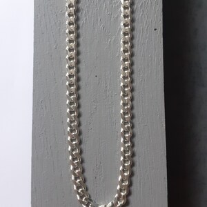 Op de afbeelding: Een zilveren curb chain ketting. De ketting is gemaakt van in elkaar grijpende schakels die een platte, rechthoekige vorm vormen.
