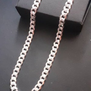 Op de afbeelding: Een zilveren curb chain ketting. De ketting is gemaakt van in elkaar grijpende schakels die een platte, rechthoekige vorm vormen.