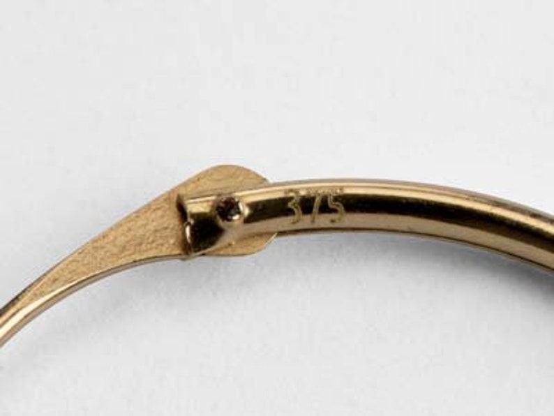 May include: Close-up of a gold hoop earring with a clasp. The earring is marked with the number "375".