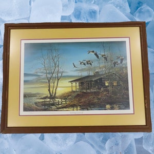 May include: Framed print of a cabin in the woods with a sunset in the background and a flock of geese flying overhead. The print is titled "Whispering Distant".