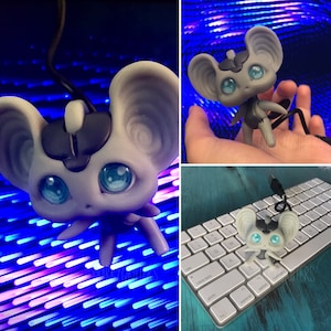 May include: A gray and white mouse-shaped USB drive with blue eyes. The drive is plugged into a keyboard and a hand is holding the drive.