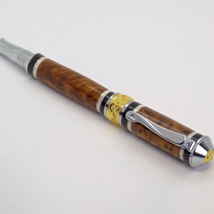 May include: A brown and gold pen with a silver clip and a decorative design. The pen has a wood grain pattern and a black and white stripe.