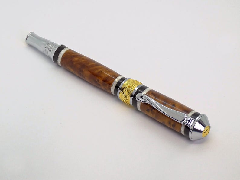 May include: A brown and gold pen with a silver clip and a decorative design. The pen has a wood grain pattern and a black and white stripe.