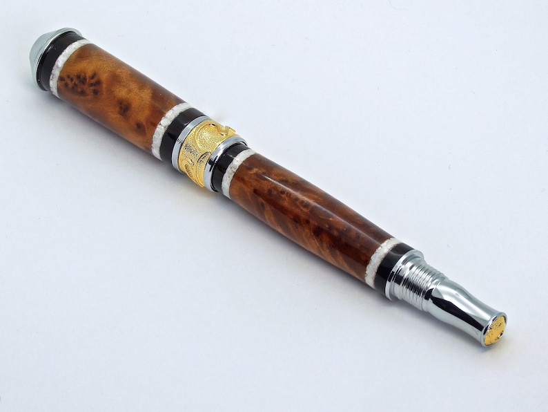 May include: A wooden pen with a brown and white burl wood design, silver accents, and a gold band. The pen has a twist mechanism.