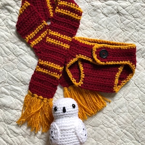 May include: A crocheted baby outfit in red and gold with a white crocheted owl toy. The outfit includes a diaper cover and a scarf with tassels.