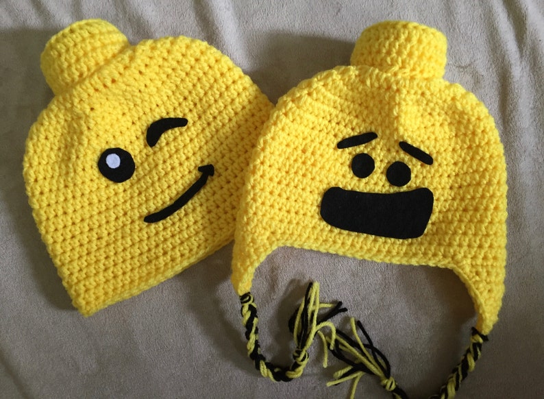 May include: Two yellow crocheted hats with black felt faces. One hat has a winking face and the other has a surprised face.