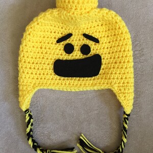 May include: Yellow crocheted hat with a black smiling face and black and yellow braided ties.