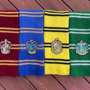 May include: Four knitted scarves with different colored stripes and Hogwarts house crests. The crests are Gryffindor, Hufflepuff, Slytherin, and Ravenclaw.