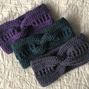 May include: Three crocheted headbands in shades of purple, teal, and gray. Each headband has a twisted knot design.