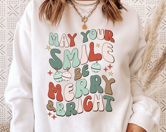 May include: White sweatshirt with a retro-style graphic that says "May your smile be merry & bright". The graphic features colorful letters and ornaments.