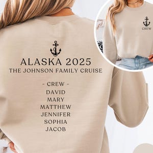 May include: A sand-colored sweatshirt with a black anchor and the text "ALASKA 2025 THE JOHNSON FAMILY CRUISE" on the back. The front of the sweatshirt has a small black anchor and the text "CREW".