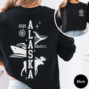 May include: Black sweatshirt with a white graphic design on the back. The design features a whale, a boat, a moose, a compass, and the text "2025 ALASKA".