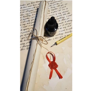 May include: A rolled up parchment paper with a red wax seal and a ribbon, a small bottle of black ink, and a yellow calligraphy pen on a white surface.