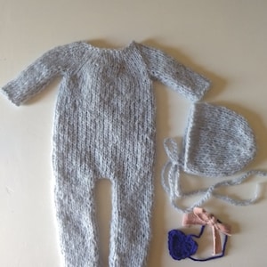 May include: A gray knitted baby outfit with a matching hat, a purple flower headband, and a pink bow.