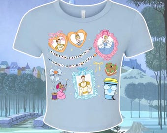 Op de afbeelding: Lichtblauw T-shirt met een grafisch ontwerp met Assepoester en Prins Charming. Het ontwerp bevat hartvormige frames, een roze frame en de tekst "A dream is a wish your heart made."