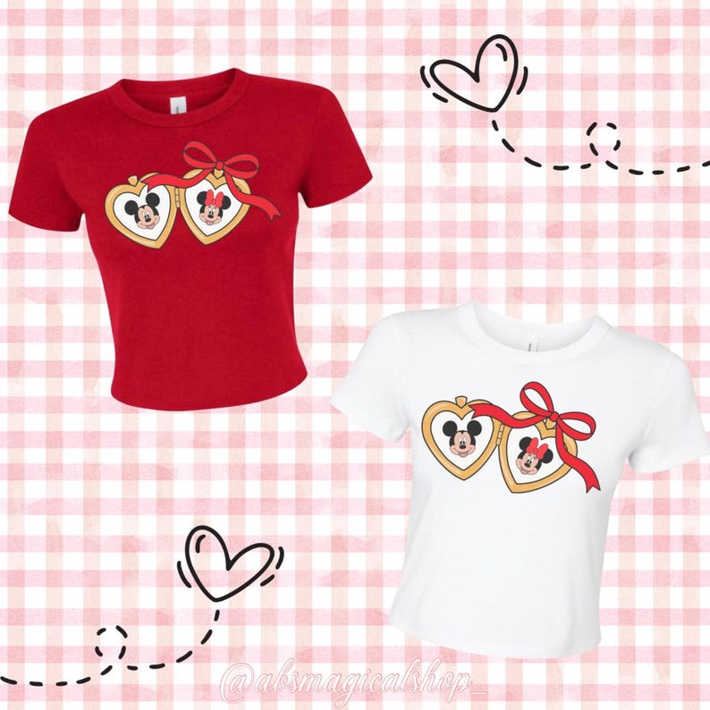 May include: Two cropped t-shirts featuring a heart-shaped locket design with Mickey and Minnie Mouse. The shirt on the left is red and the shirt on the right is white.