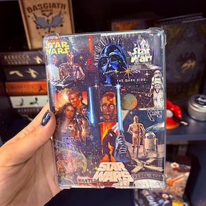 May include: A clear phone case featuring a collage of Star Wars imagery, including Darth Vader, C-3PO, and R2-D2. The case has a holographic, glittery effect and includes the text "Star Wars" and "The Dark Side."
