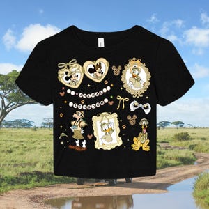 May include: Black t-shirt with a colourful graphic print featuring Disney characters Mickey Mouse, Donald Duck, and Goofy in safari outfits. The text "Animal Kingdom" is printed on the shirt.