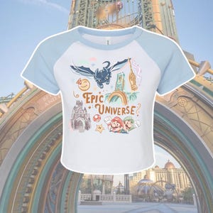 May include: White and pale blue crop top with a graphic design featuring a dragon, a wand, a castle, and the text "Epic Universe?" The shirt also includes images of Mario and Luigi.