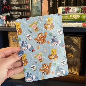 May include: A light blue rectangular sticker featuring cartoon characters in Star Wars and Winnie the Pooh themes. The design includes characters like Winnie the Pooh as Obi-Wan Kenobi, Piglet as Yoda, and Tigger as a Jedi. Other elements include lightsabers and Stormtrooper helmets.