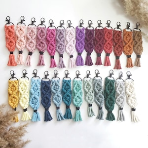May include: A collection of 25 colorful macrame keychains with black metal rings. The keychains are made with a variety of colors, including pink, blue, green, yellow, red, and purple. The keychains are all about 5 inches long.