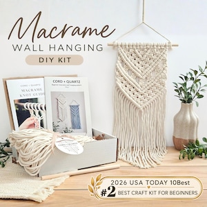 May include: A macrame wall hanging DIY kit featuring a white cotton cord, a wooden dowel, and instructional guides labeled CORD + QUARTZ. The kit includes a finished macrame wall hanging with a chevron pattern and fringe, plus a box.