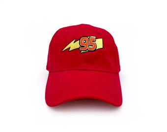 May include: A red baseball cap featuring a gold lightning bolt and the number 95 in gold and white. The cap is made of a soft material and has a curved brim. The design is centered on the front of the cap.