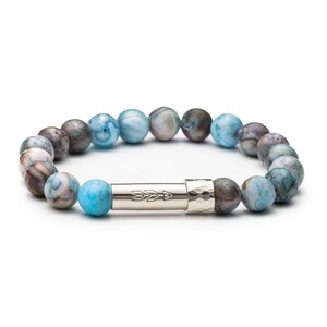 Peut inclure: Un bracelet en agate bleu et gris avec un charme en argent en forme de flèche. Le bracelet est fait de pierres naturelles et a un aspect unique et texturé.