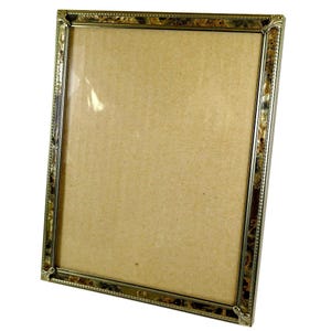 May include: A rectangular picture frame with a gold-colored metal frame. The frame has a decorative pattern along the edges and corners. The frame holds a tan-colored backing and a clear glass or plastic cover.