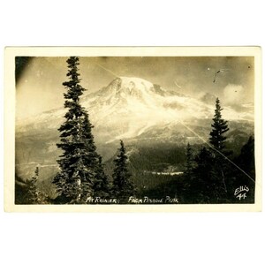 May include: Vintage black and white postcard featuring a scenic view of Mount Rainier from Pinnacle Peak. The image shows a snow-capped mountain in the background, with evergreen trees in the foreground. The text "Mt. Rainier From Pinnacle Peak" is printed at the bottom.