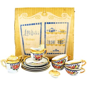 May include: A vintage children's play set of dishes, featuring a teapot, creamer, cups, saucers, and plates. The dishes are white with colorful floral designs and gold trim. The box reads "Little Hostess dishes for play."