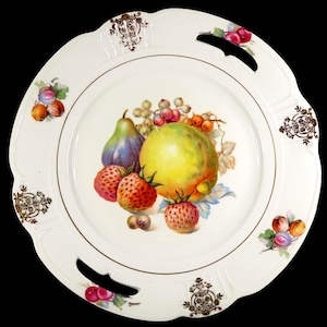 May include: A white porcelain serving plate with a scalloped edge and two integrated handles. The center features a colorful illustration of a pear, strawberries, and grapes. The rim is decorated with gold filigree accents and small fruit motifs.