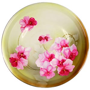 May include: A round, decorative plate with a light yellow interior and a brown rim. The plate is adorned with a floral design featuring pink and red flowers with green stems and leaves. The flowers are clustered in the center and scattered around the plate.
