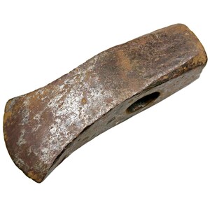 Puede incluir: Una cabeza de maza de metal oxidado y desgastado. La cabeza es rectangular con un filo biselado y un ojo redondo para el mango. El metal tiene un aspecto moteado marrón y plateado, lo que indica edad y uso.