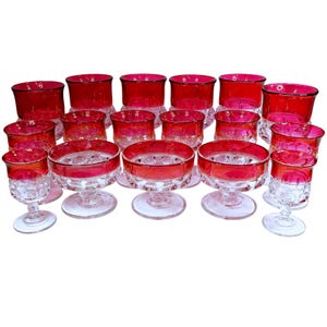 May include: A collection of vintage ruby red glassware. The set includes various sizes of stemmed glasses, bowls, and tumblers. The rims of the glasses are a deep red, contrasting with the clear, patterned bases. A classic and elegant set.