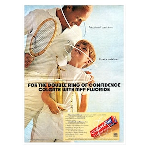 Peut inclure: Publicité vintage pour Colgate avec un homme et un garçon en tenue de tennis blanche, avec une raquette et un trophée. L'annonce promeut Colgate avec MFP Fluoride, avec du texte sur la confiance en soi.