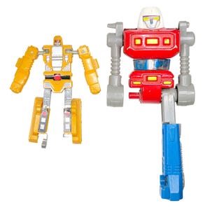 May include: Two vintage toy robots. One is yellow and silver, with articulated arms and legs. The other is red, white, blue, and gray, with a blocky design. Both are standing against a white background.