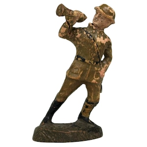 May include: A vintage figurine of a soldier in a green uniform, holding a horn to his mouth. The figurine has a weathered appearance with visible paint chipping, suggesting age. The base is dark green.