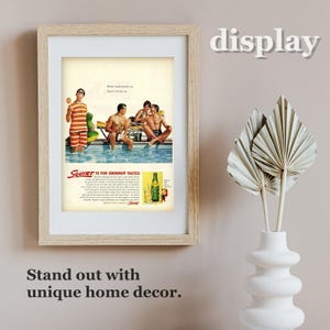 K&ouml;nnte beinhalten: Gerahmter Vintage-Werbedruck mit einem Retro-Bild von M&auml;nnern an einem Pool, mit dem Text "Squirt is for Grownup Tastes". Der Druck befindet sich in einem hellen Holzrahmen, mit den Worten "display" und "Stand out with unique home decor" im Hintergrund.