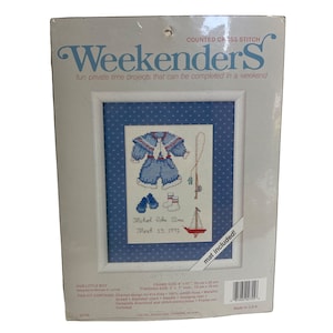 Puede incluir: Un kit de punto de cruz contado para un bebé. El kit incluye un traje de marinero azul y blanco, una caña de pescar, un velero y un par de guantes azules. El kit también incluye una alfombra y el texto "Michael John Sims March 15, 1991".